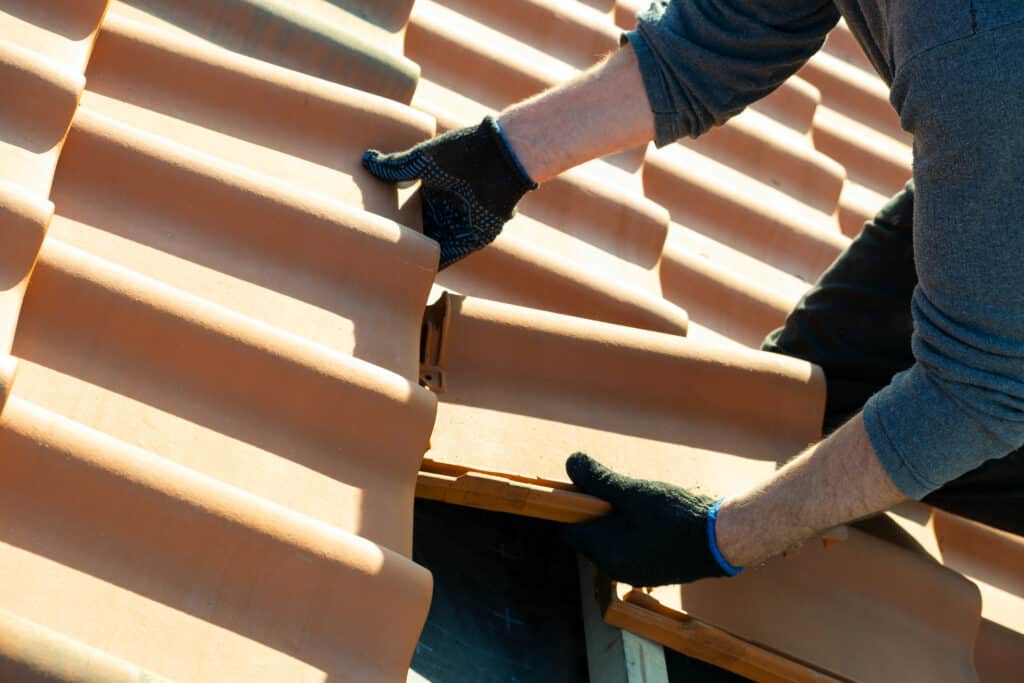 Pose de tuiles en terre cuite par un couvreur, lors de la rénovation d’une toiture traditionnelle dans le Pays de Caux