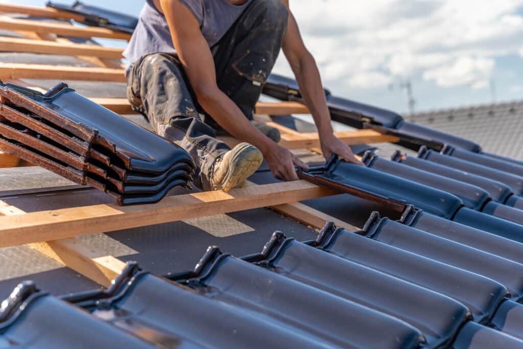 Un couvreur professionnel en plein travail de pose de tuiles en céramique noires sur une charpente en bois, lors d’un chantier de rénovation de toiture à Doudeville, réalisé par l’entreprise Caux’ Charpente, spécialisée en couverture et charpente.