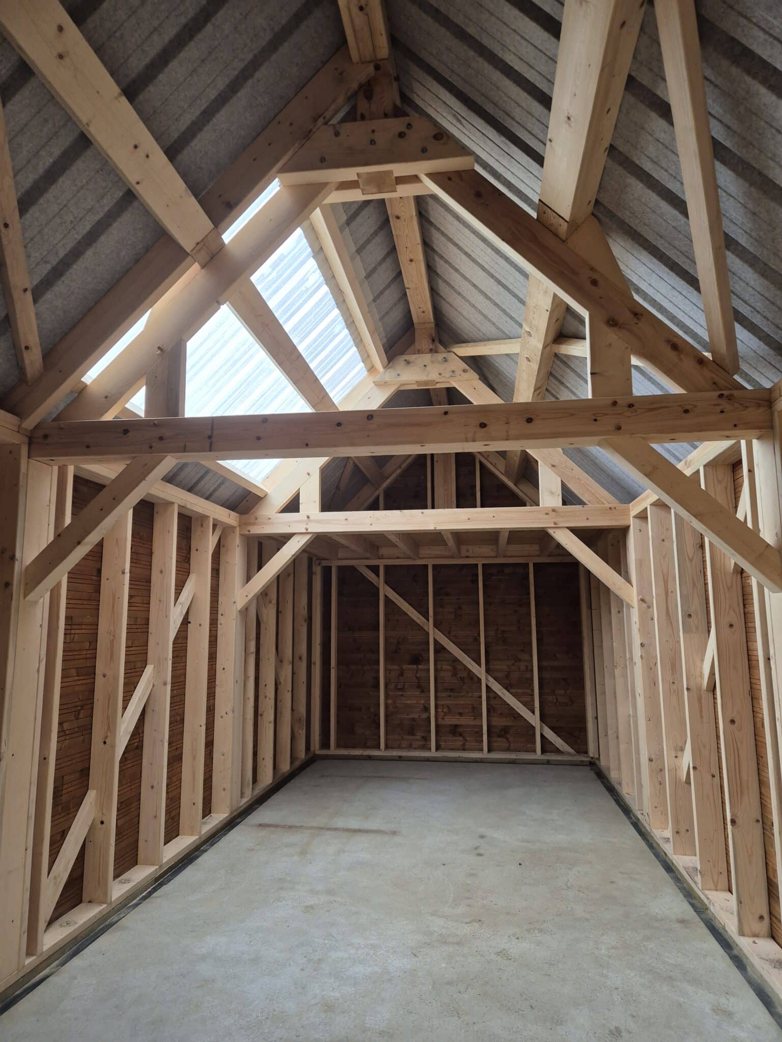 Montage d’une charpente traditionnelle en bois réalisée par un charpentier à Doudeville, avec ossature apparente sous toiture bac acier et puits de lumière intégré.