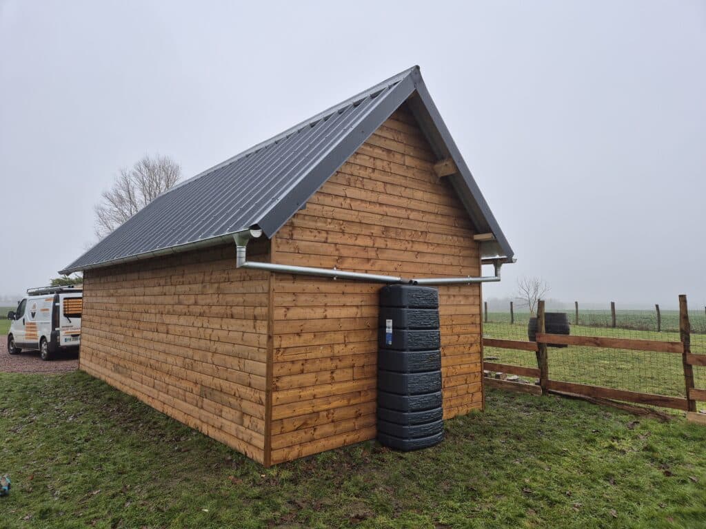 Construction d’un bâtiment annexe en bardage bois avec couverture en bac acier, réalisée à Doudeville par un charpentier, incluant système de récupération d’eau et finitions de zinguerie.
